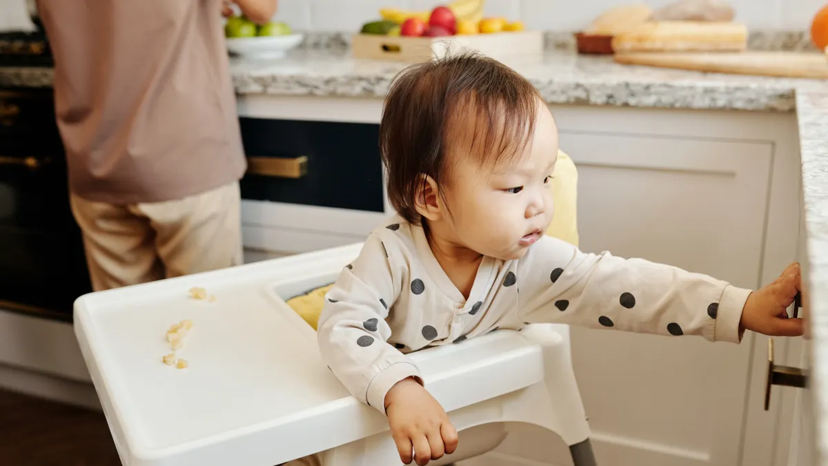 Toddler standing at a kitchen cabinet and reaching for the door