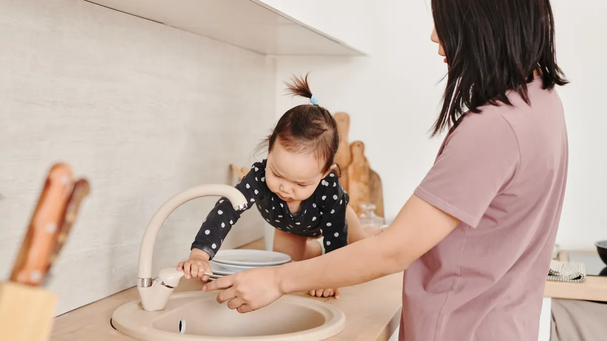 Adult helping toddler at kitchen sink